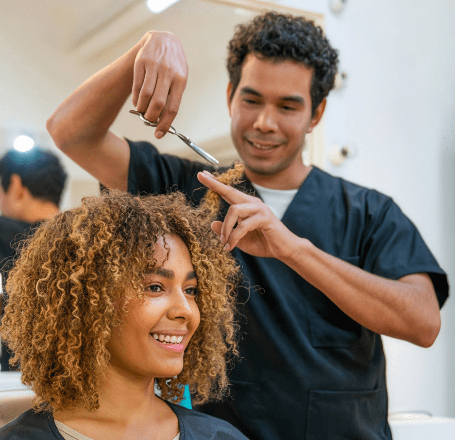 Hairstylist trimming a smiling client’s curly hair in a salon