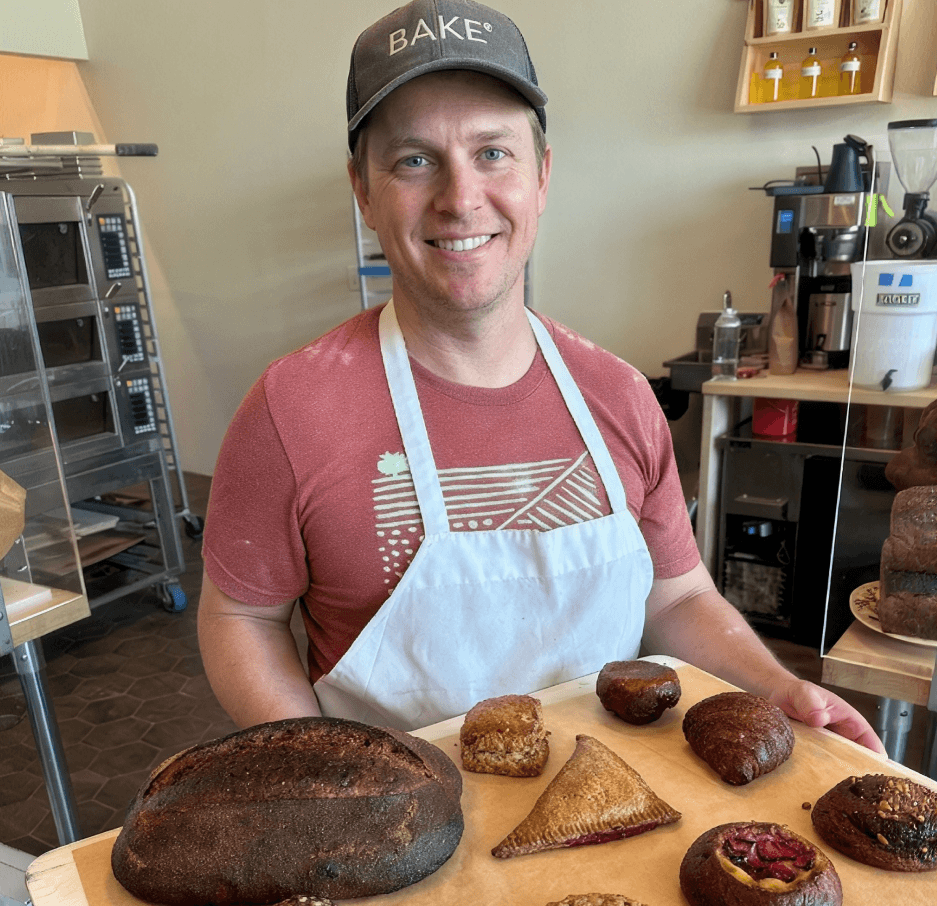 Smiling baker holding a tray of fresh bread and pastries in a bakery