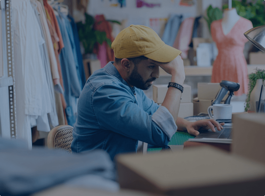 Small business owner looking stressed while working on a laptop in their shop